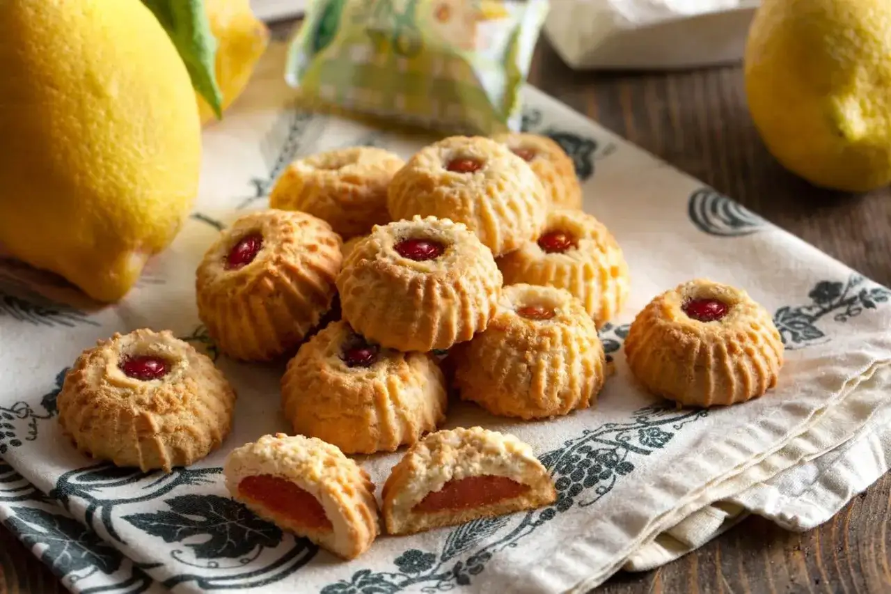 Biscotti tipici italiani con ripieno di marmellata, su un tovagliolo decorato, con limoni sullo sfondo.