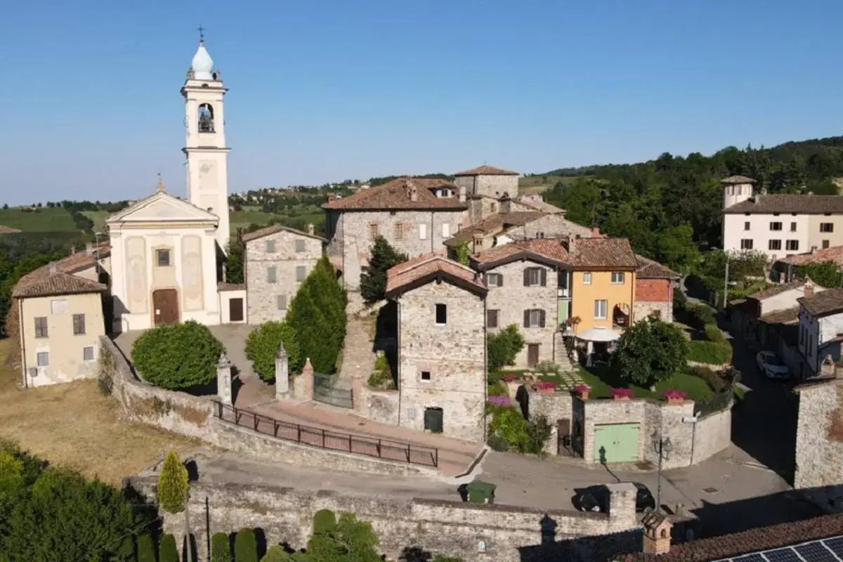 Un incantevole borgo in provincia di Pavia, con una chiesa dal campanile svettante, case in pietra e tetti rossi, immerso nel verde delle colline.