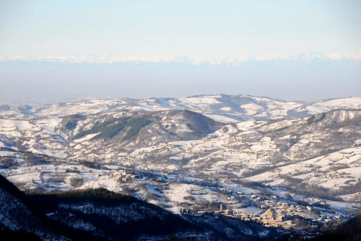Paesaggio innevato con borghi aggrappati alle colline. Il monte Penice, coperto di neve, domina la vista.