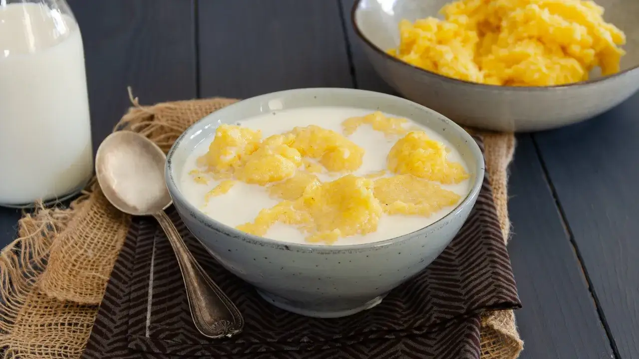 Una ciotola di polenta e latte, un piatto confortante e tradizionale. Accanto, una bottiglia di latte e un cucchiaio d'argento.