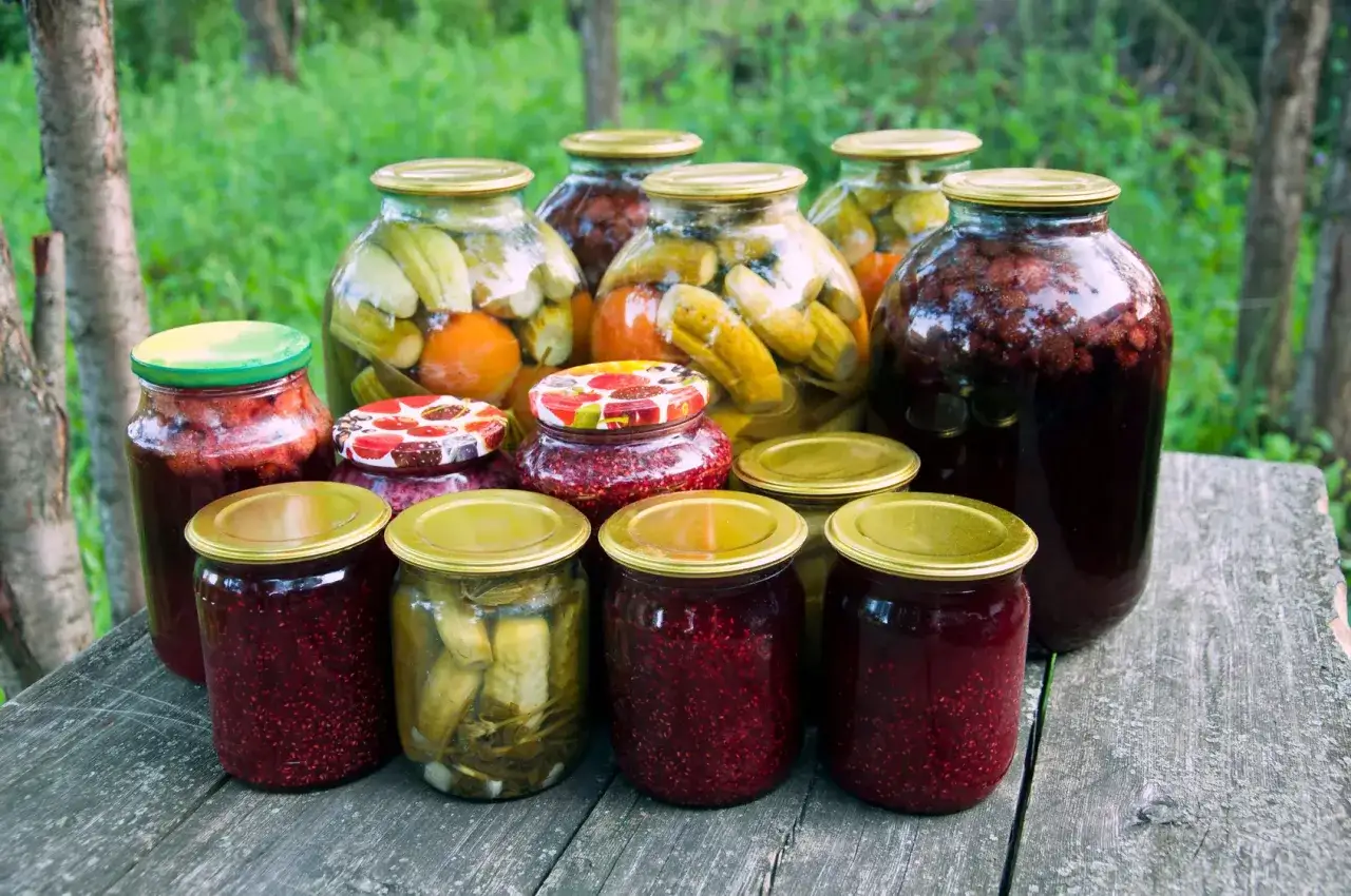Vasi di classici frutti di conserva e sottaceti, pronti per l'inverno, su un tavolo di legno all'aperto.