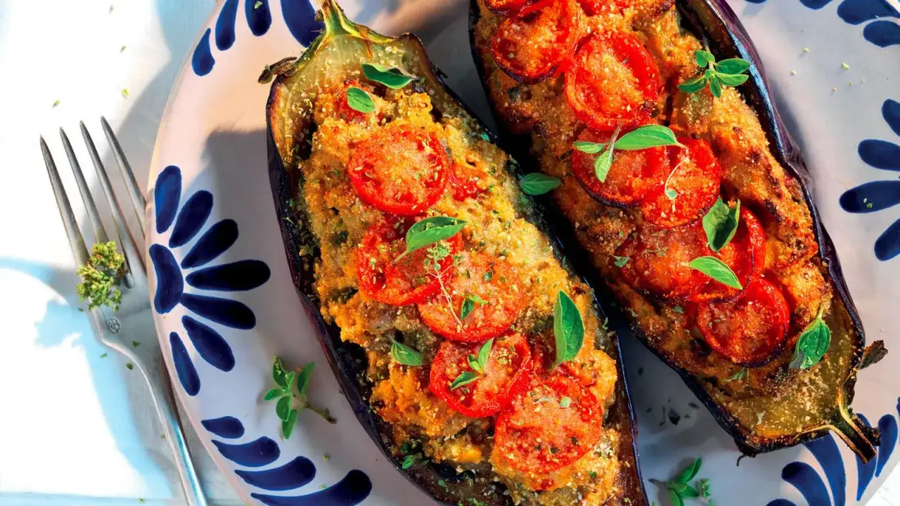 Melanzane ripiene al forno, un classico delle ricette con melanzane, guarnite con pomodoro e basilico fresco.