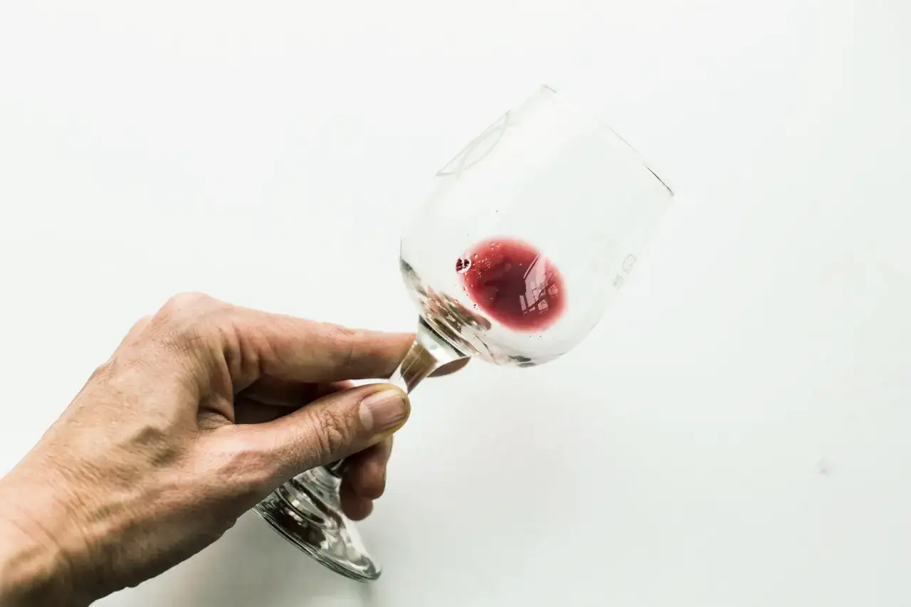 Mano che tiene un bicchiere di vino rosso, con residui che ricordano l'acido tartarico, simbolo della qualit&agrave; del vino.