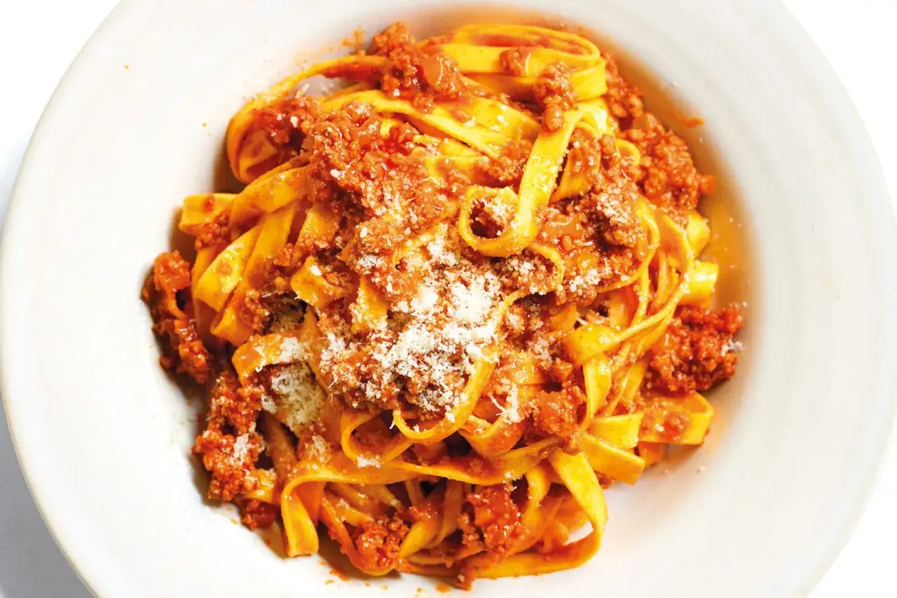 Un piatto invitante di pasta asciutta con rag&ugrave; ricco e abbondante parmigiano grattugiato, pronto per essere gustato.