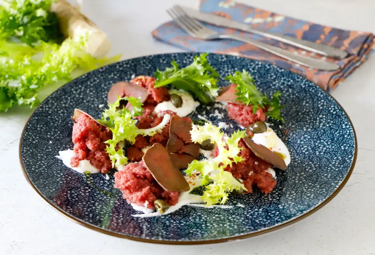 Piatto di carne cruda finemente tritata, guarnito con lattuga croccante, capperi e una salsa bianca cremosa.
