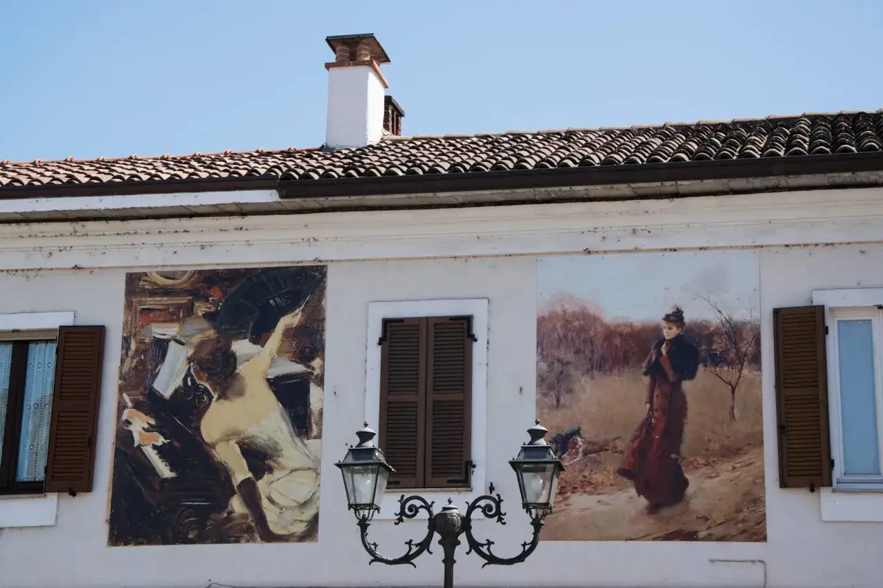 Affreschi d'arte su un muro a Gravellona Lomellina: una donna al pianoforte e un'altra in un paesaggio autunnale.