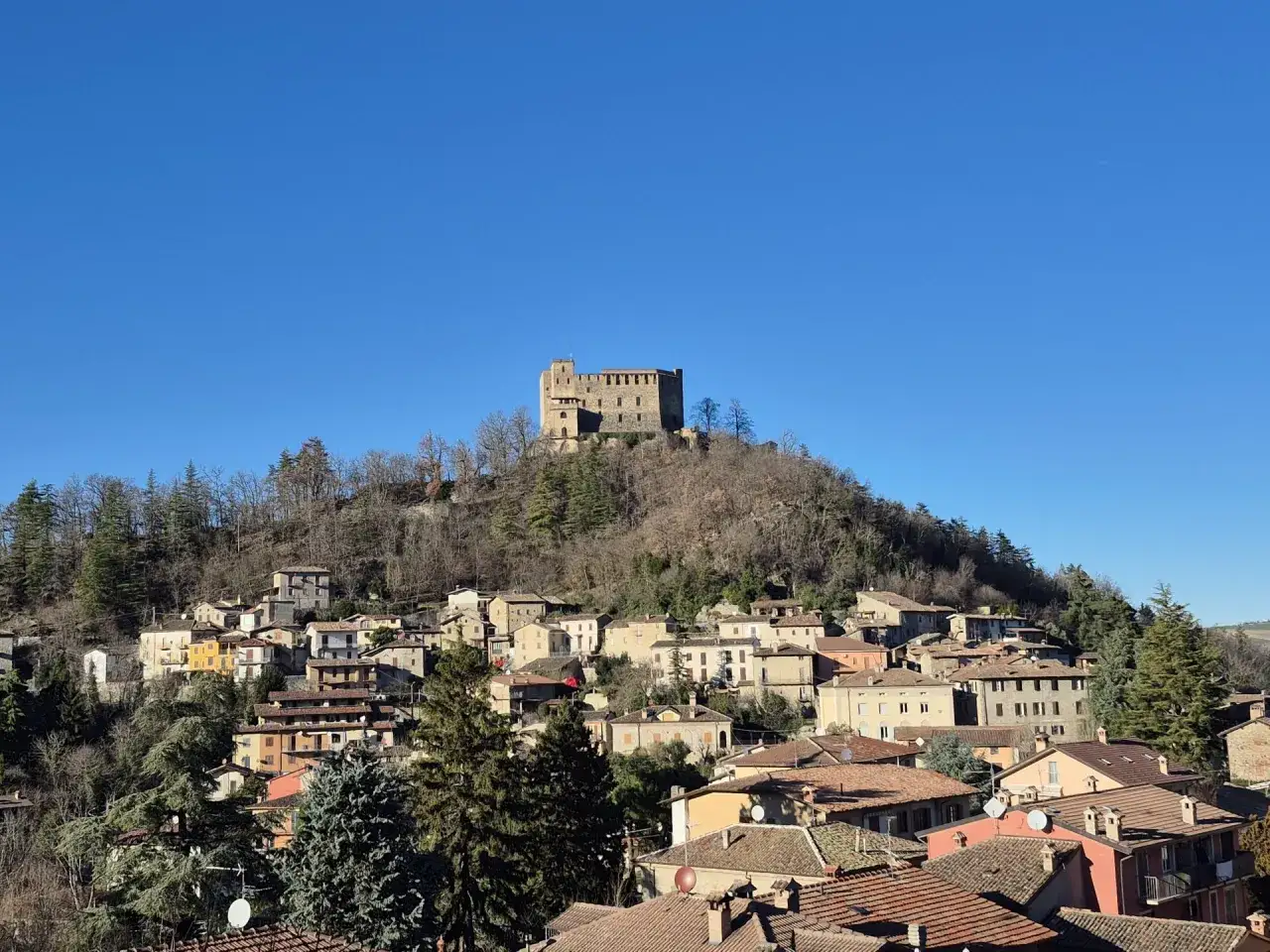 Castello di Zavattarello domina il borgo collinare. Un luogo incantevole da scoprire, tra case in pietra e tetti rossi sotto un cielo azzurro.