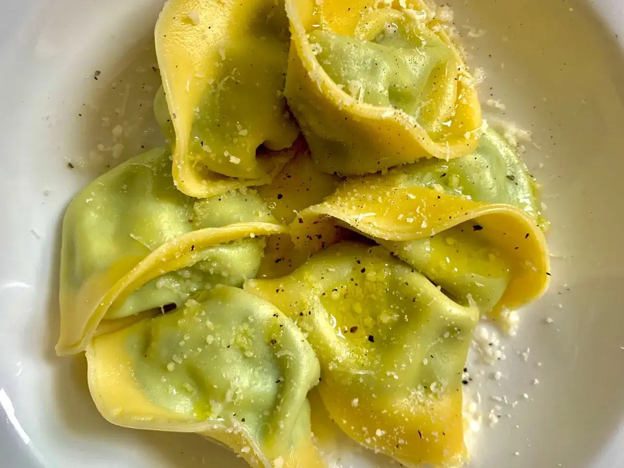 Un piatto di ravioli italiani verdi e gialli, conditi con olio, pepe e parmigiano grattugiato.