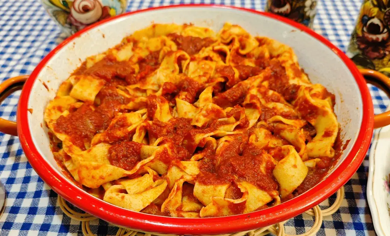 Pappardelle al rag&ugrave; di papera, un piatto ricco e saporito, servito in una ciotola rossa su una tovaglia a quadri blu.