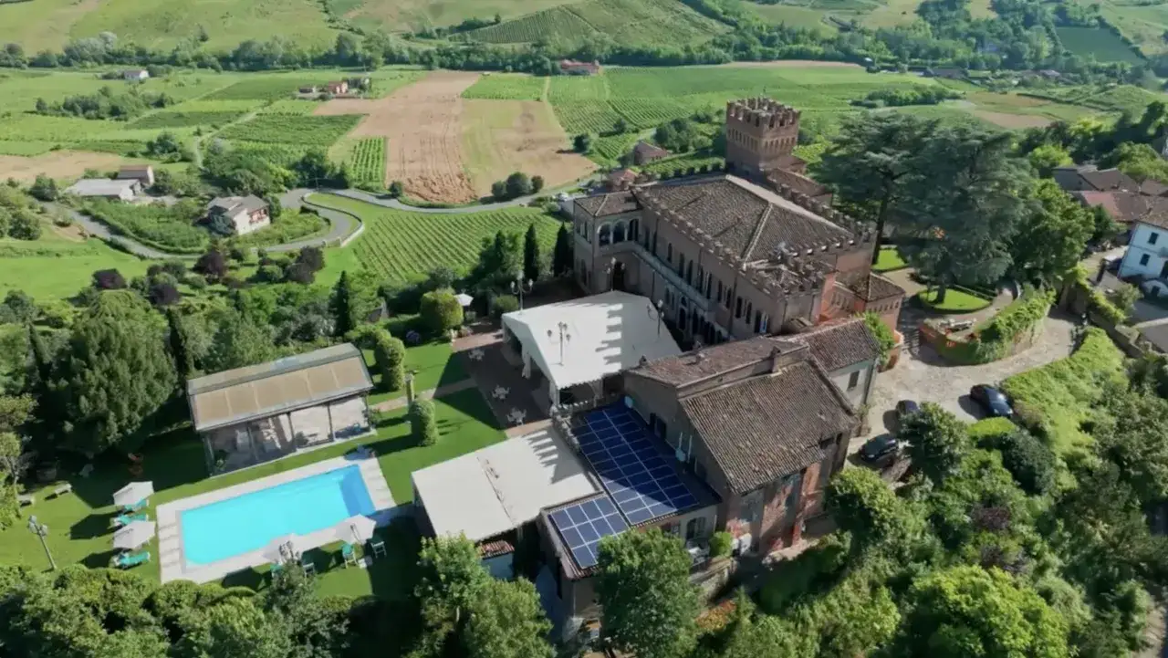 Castello di Mornico Losana immerso tra vigneti e colline verdi, con piscina e pannelli solari.