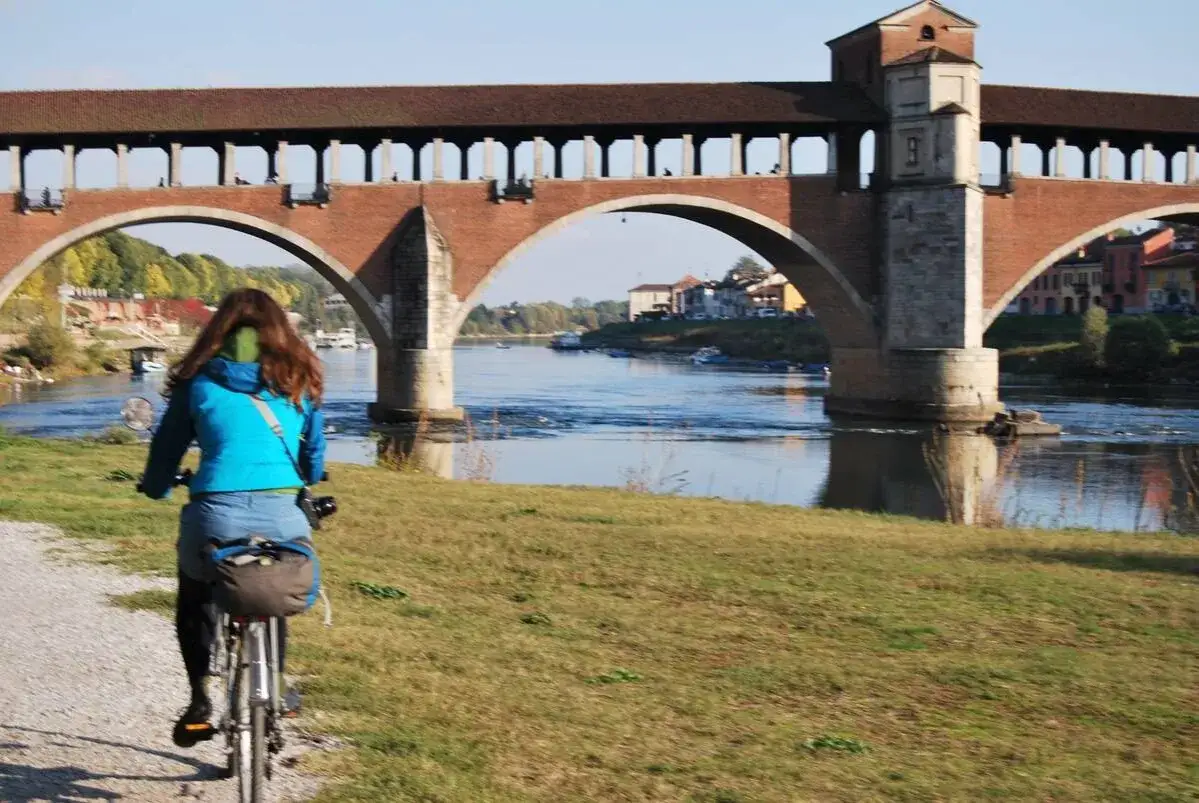 Ciclista sulla ciclabile Milano Pavia, con il Ponte Coperto di Pavia sullo sfondo.