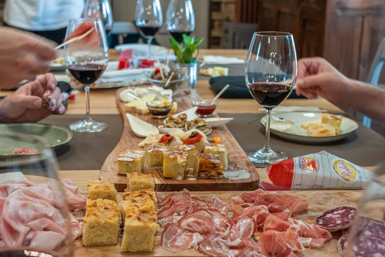 Un tavolo imbandito con salumi, formaggi e stuzzichini, accompagnati da calici di vino rosso dolce. Nomi di vini come Porto o Recioto potrebbero evocare questa scena.