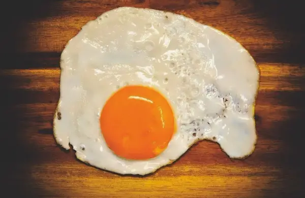 Un uovo in cereghin, cotto alla perfezione, con un tuorlo arancione brillante su un tagliere di legno scuro.