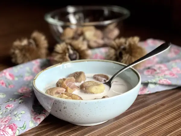 Una ciotola di castagne al latte, un dolce autunnale cremoso e confortante, con ricci di castagne sullo sfondo.